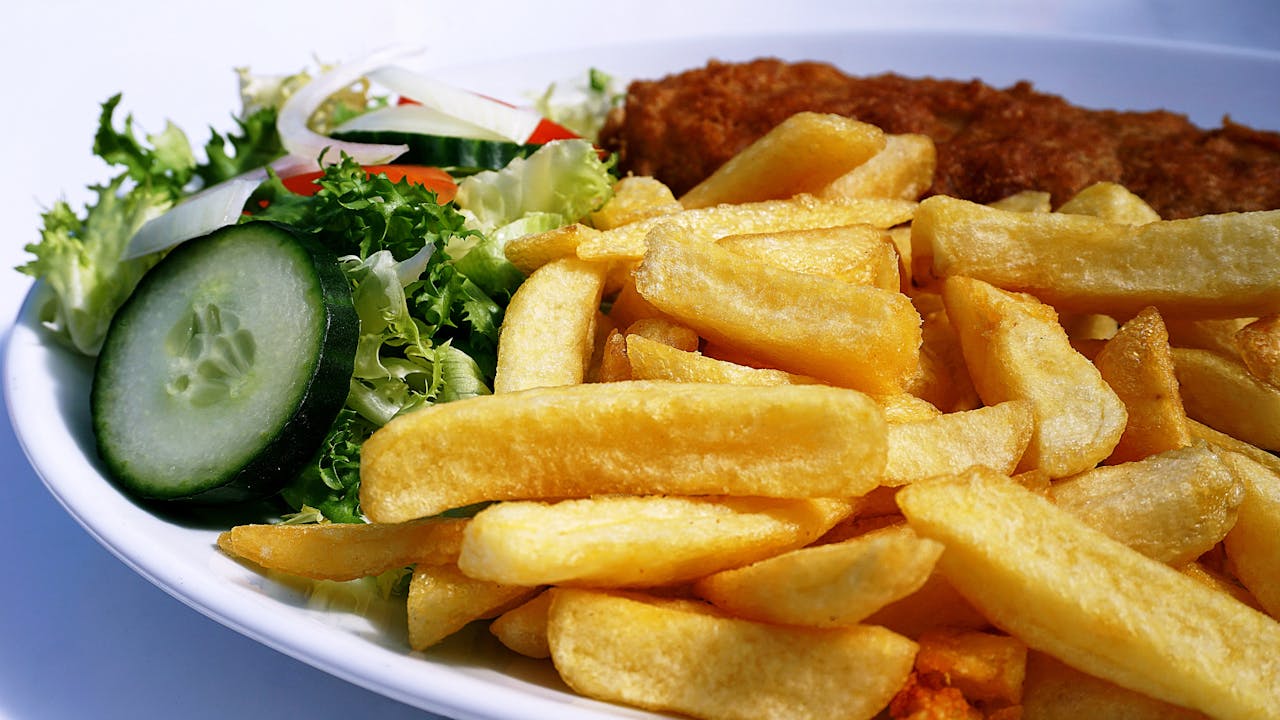 Home Golden fish and chips served with a fresh cucumber and lettuce salad on a plate.