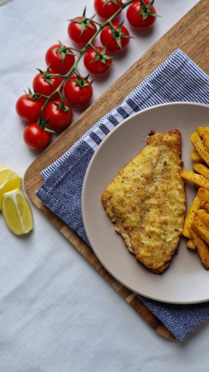 Home Delicious crispy fish with seasoned chips and fresh cherry tomatoes on a wooden board.